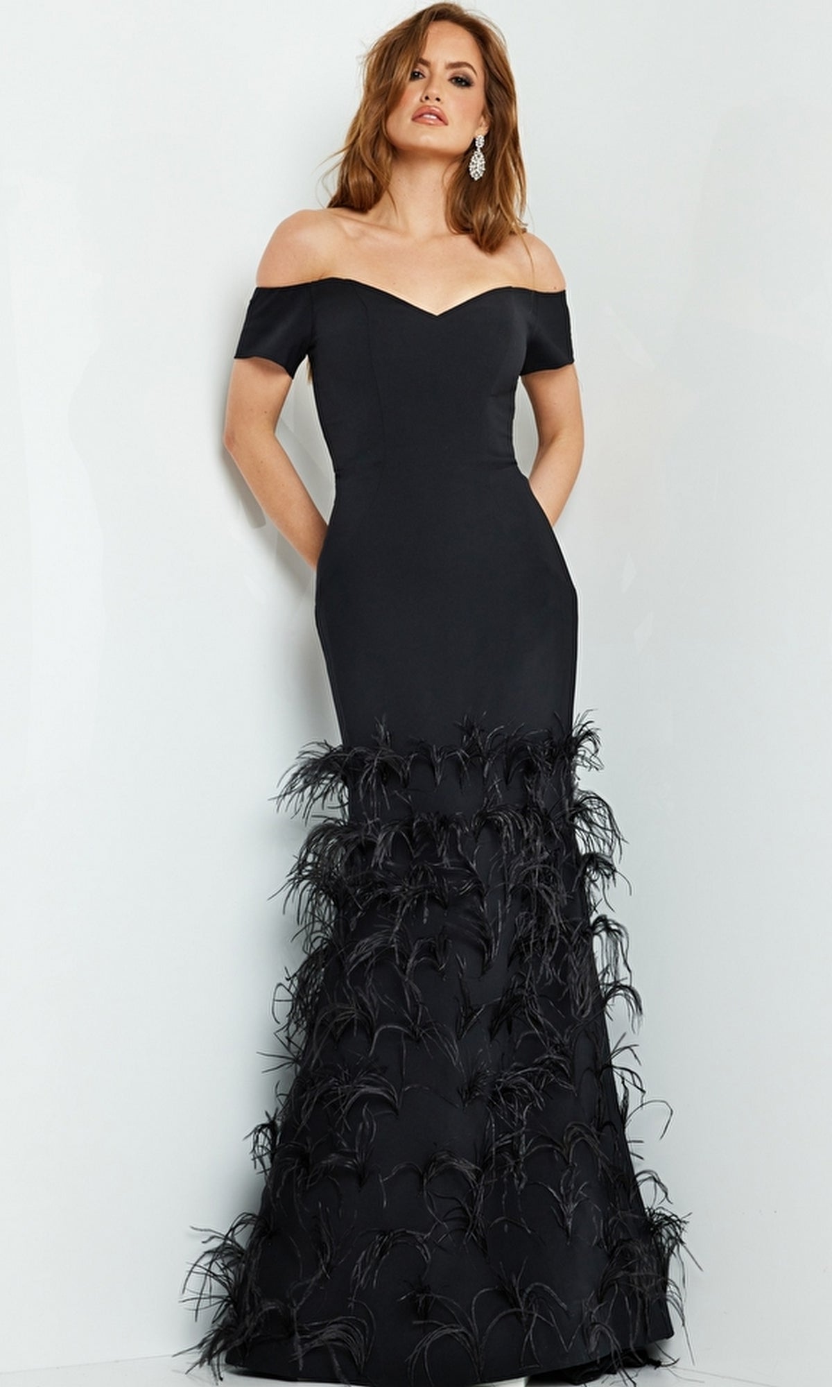 A woman models the Jovani 08384 Off-Shoulder Feather Mermaid Gown, featuring a fitted silhouette and feather details on the lower half, set against a plain white background.